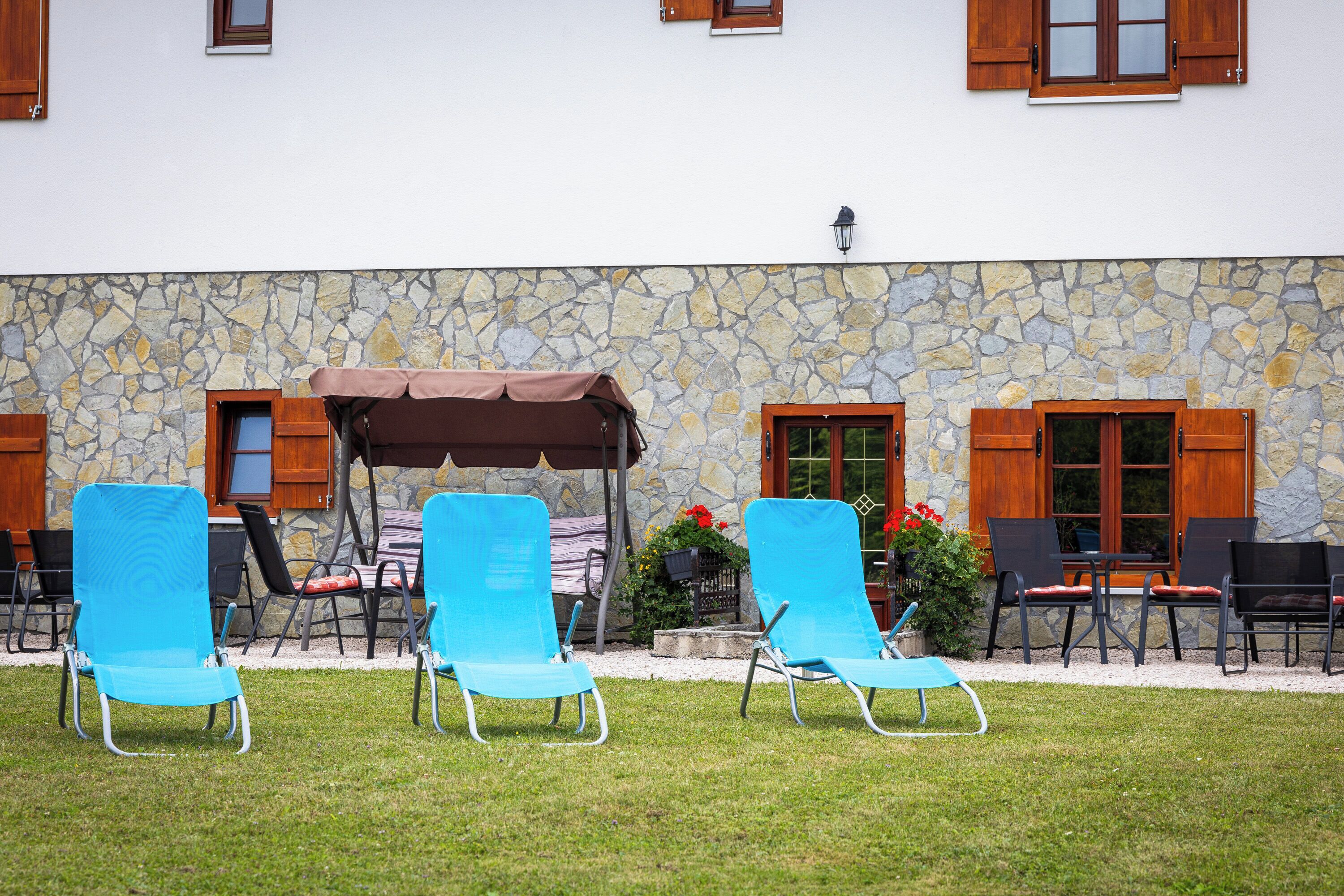 A stone building with a patio area featuring blue lounge chairs and wooden tables.
