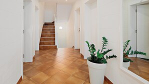 Un pasillo con una escalera, paredes blancas y una planta en maceta.