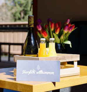 A wooden table with a sign reading "Herzlich willkommen" and two bottles, one dark and one yellow, on a tray.