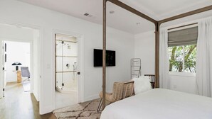 Un dormitorio con una cama grande, un televisor montado en la pared, techo de madera y una ventana con cortinas.