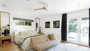 Un dormitorio con cama, sofá, ventana grande y ventilador de techo.