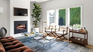 Una sala de estar moderna con chimenea, asientos cómodos, una mesa de centro y un ventanal con vistas a la vegetación.
