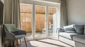 A living room with a sofa, a chair, and a sliding glass door leading to a wooden deck. - Beach Mews | Central | Family house | Parking (Broadstairs)