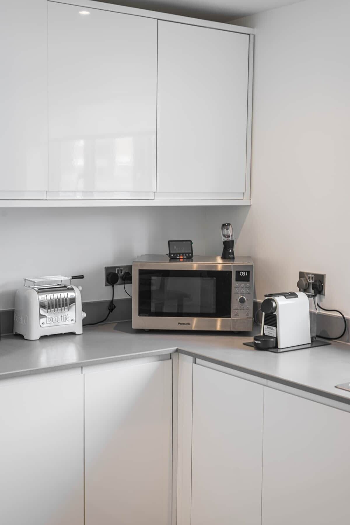 Een keuken met witte kastjes, een broodrooster, een magnetron en een koffiezetapparaat.