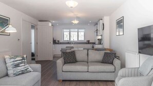 A modern living room with a grey sofa, a coffee table, and a dining area with a kitchen in the background. - Beach Mews | Central | Family house | Parking (Broadstairs)