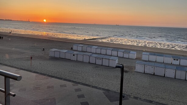 Een strand met vakantiehuisjes langs de kust, een heldere lucht en de zon die in de oceaan ondergaat.