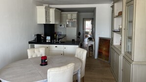 Een compacte keuken met witte kasten, een eettafel met vier stoelen en uitzicht op de aangrenzende slaapkamer.