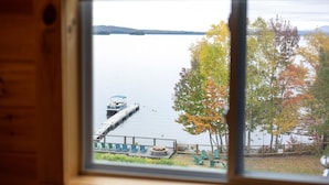 Vista de un lago con un muelle y sillas, a través de una ventana con estructura de madera.