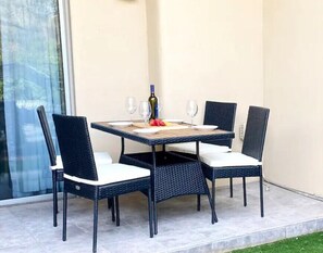 A dining table with four chairs, a bottle of wine, and two glasses on a patio with a glass door and a concrete floor. - Location, Leisure, & Luxury (Scottsdale)