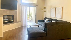 Een moderne woonkamer met een hoekbank, een flatscreen televisie aan de muur en een open haard.