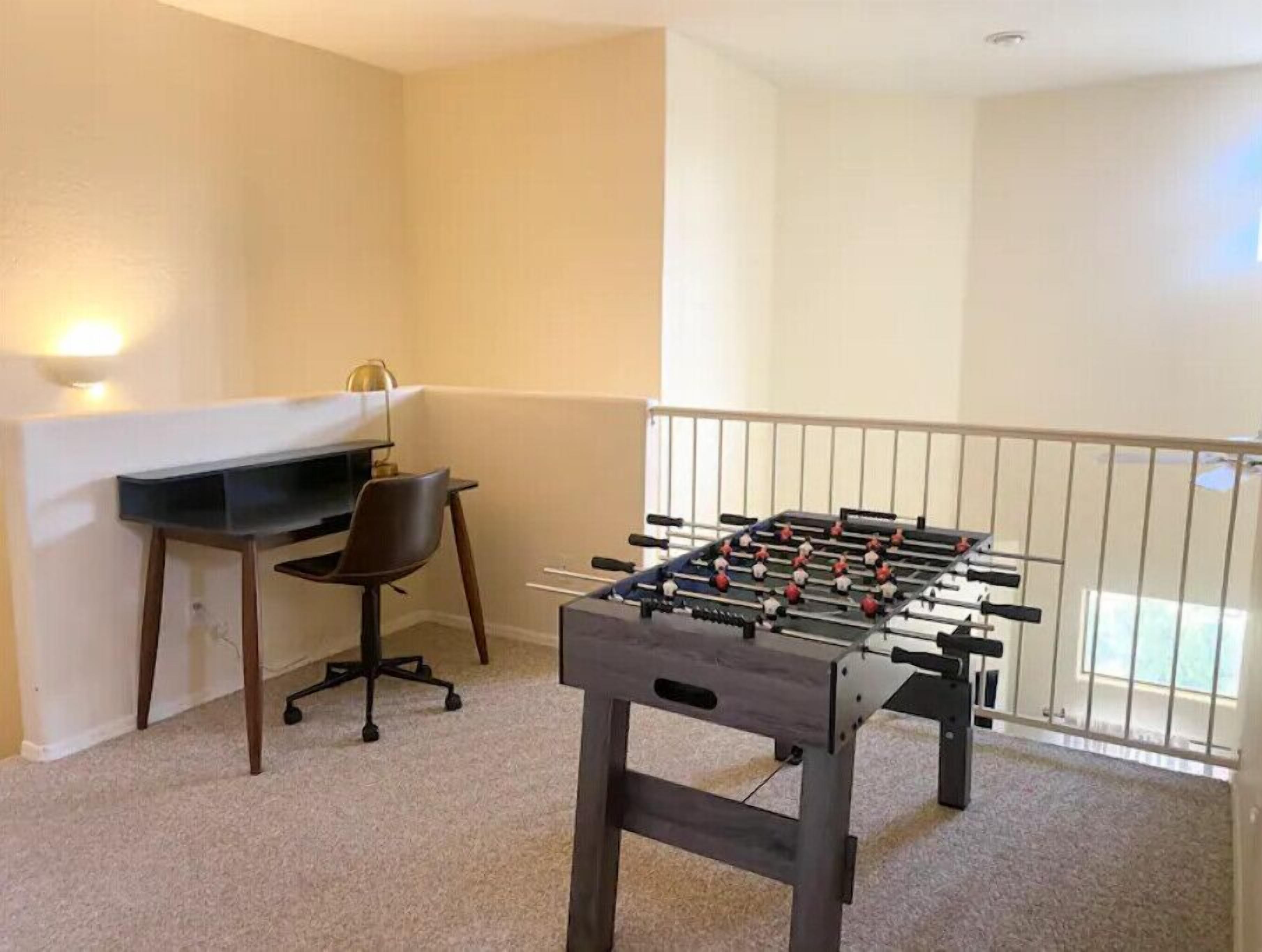 A room with a foosball table, a desk, and a chair.
