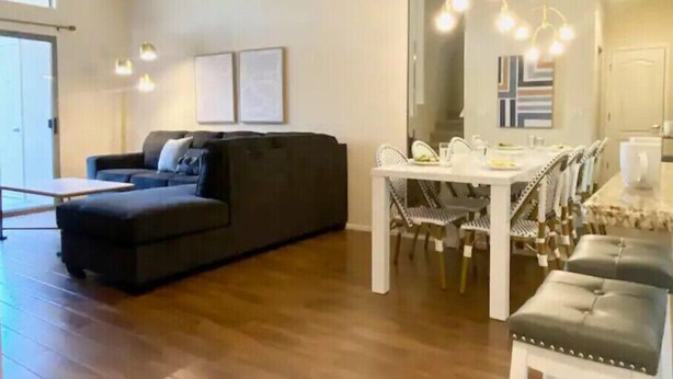 Een moderne woonkamer met een donkergrijze bank, een eettafel met stoelen en een kroonluchter.