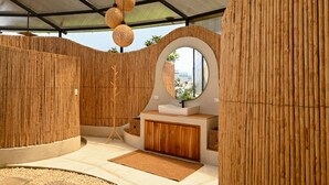 A modern bathroom with bamboo walls, a round mirror, and a wooden vanity. - ALMA Glamping  (San Antonio)