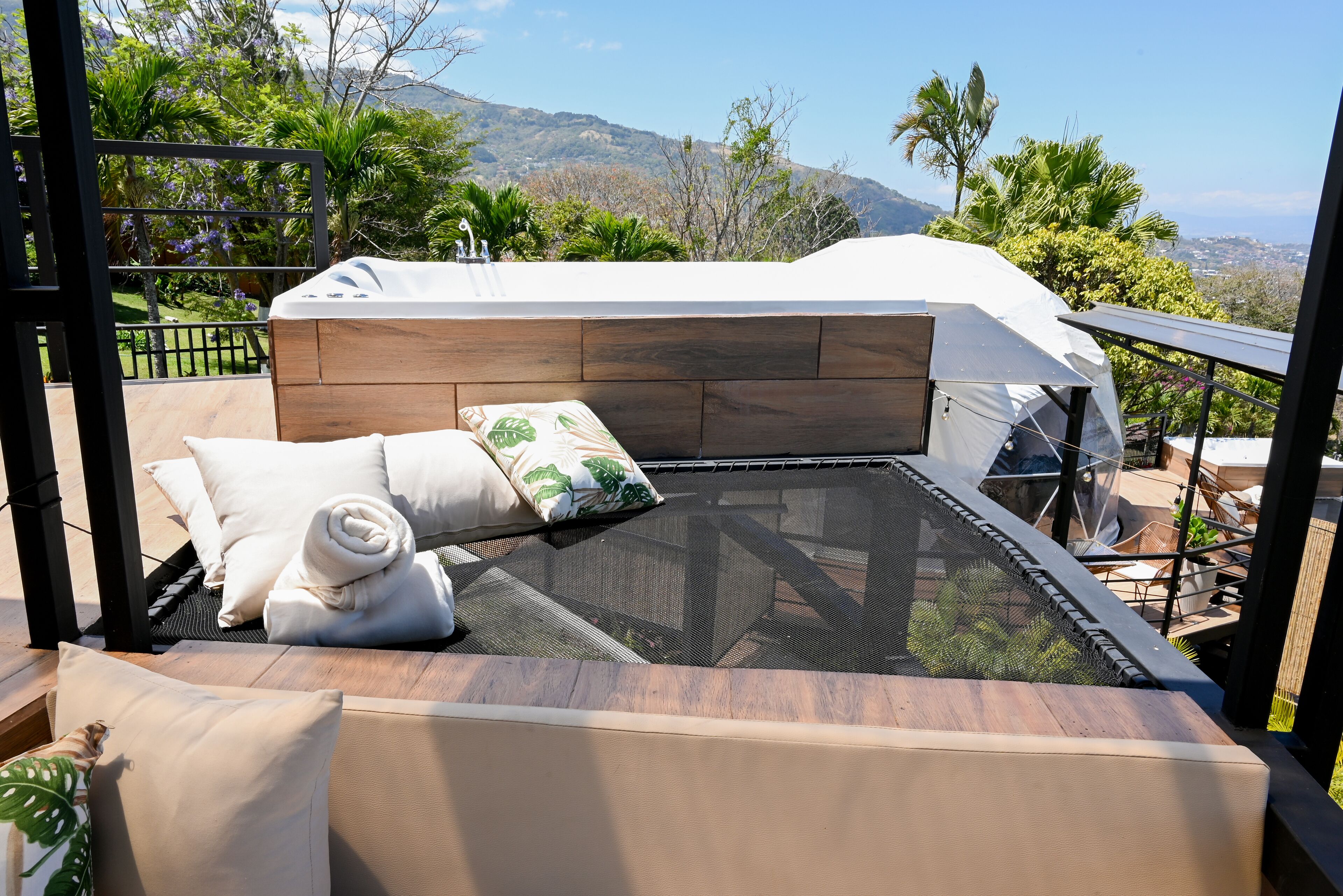 A balcony with a glass enclosure, wooden flooring, and a bed with white bedding and a rolled towel.