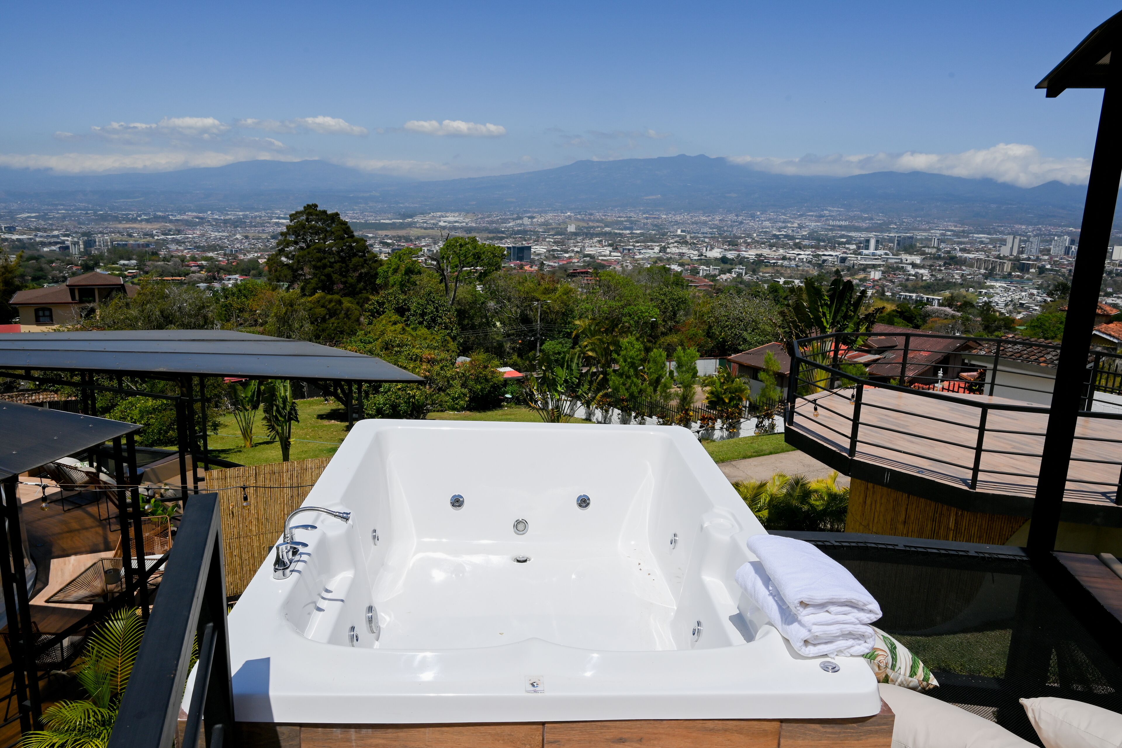 Un bain à remous avec vue sur la ville, entouré de verdure et doté d’une terrasse en bois.