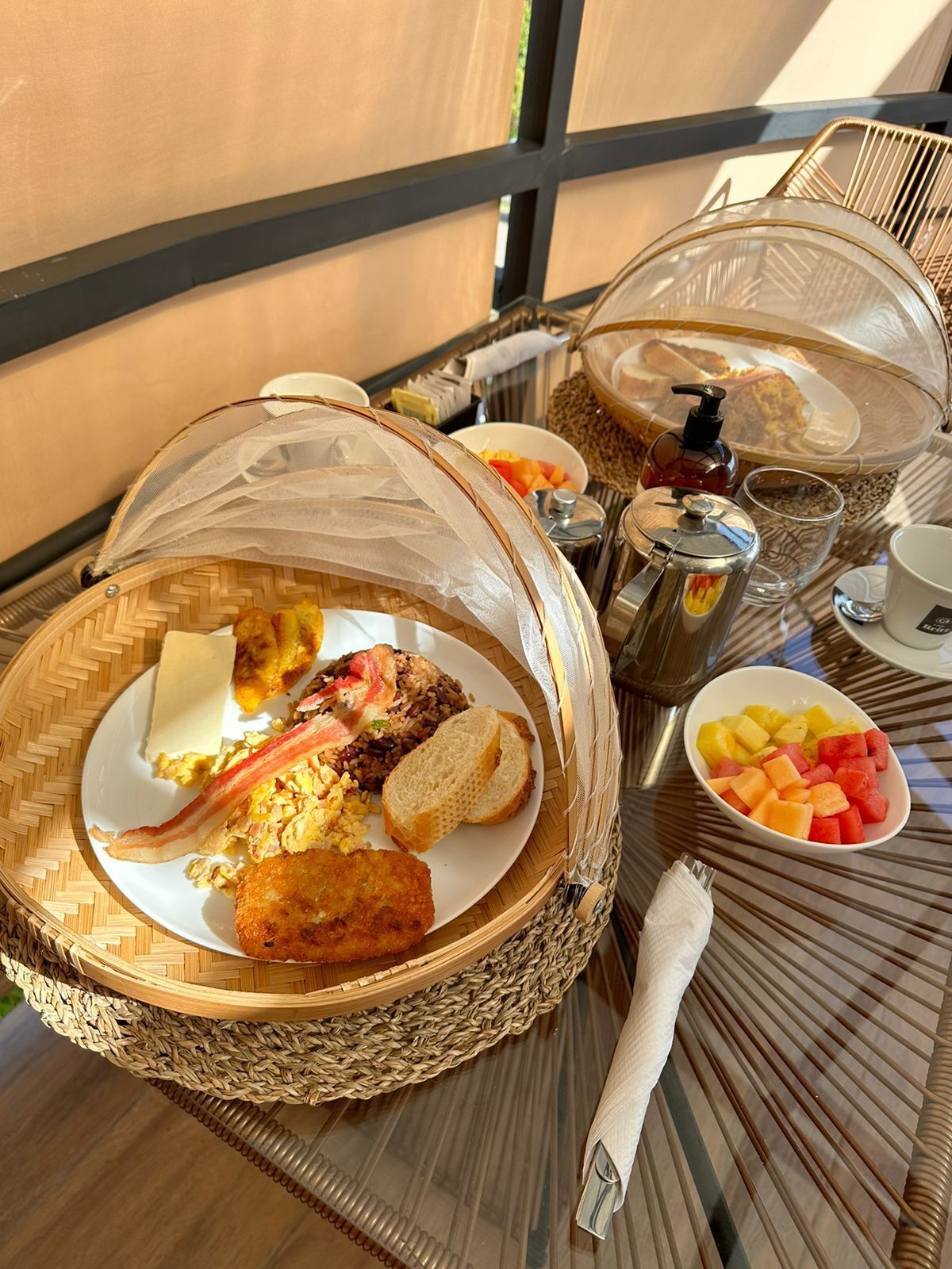 A breakfast buffet with various dishes, including fried items, eggs, and fruits, served on a table with a glass top.