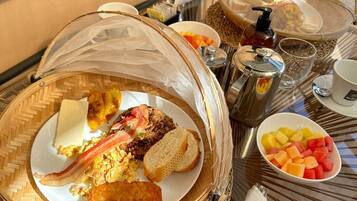 A breakfast buffet with various dishes, including fried items, eggs, and fruits, served on a table with a glass top.