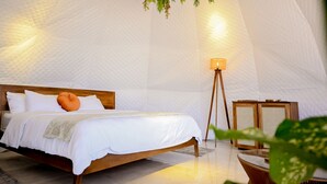 A bedroom with a bed, a bedside lamp, and a hanging plant. - ALMA Glamping  (San Antonio)