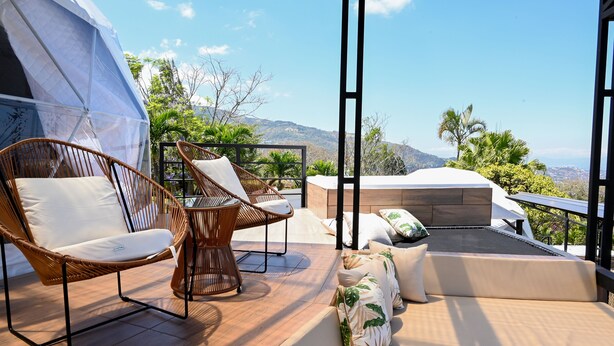 A terrace with wicker chairs, a sofa, and a hot tub overlooking a mountainous landscape. - ALMA Glamping  (San Antonio)