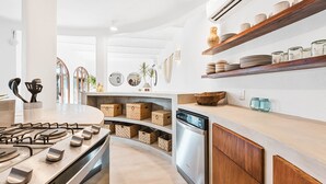 Una cocina moderna con estufa a gas, lavavajillas integrado y estantes abiertos con platos y frascos.