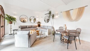 Una sala de estar moderna con un sofá seccional, una mesa de comedor con sillas de mimbre y un espejo grande en la pared.