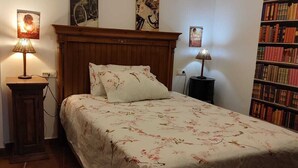 Una camera da letto con una testiera in legno, una coperta con motivi floreali, due lampade ai comodini e una libreria piena di libri.