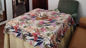 Un'area pranzo con un tavolo ricoperto da una tovaglia floreale, una poltrona verde e un quadro che raffigura una veduta cittadina.