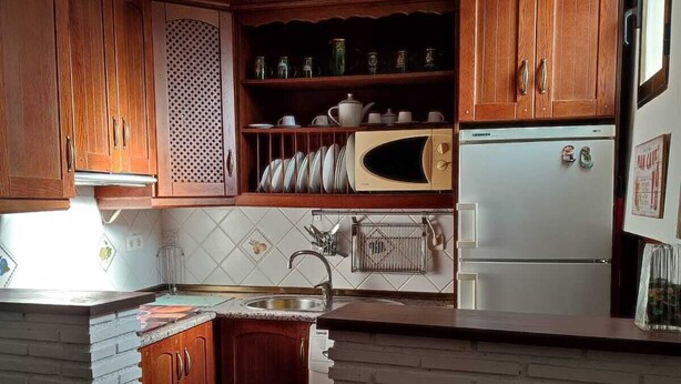 Una cucina con mobili in legno, un forno a microonde, un frigorifero e una lampada a sospensione.
