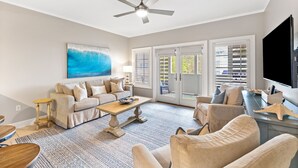 Un salon spacieux doté d’un ventilateur de plafond, d’un grand tableau, d’un canapé, d’une table basse et d’un téléviseur.