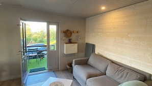 A modern living room with a beige sofa, a white coffee table, and a glass door leading to an outdoor area with a table and chairs. - The family cabin (Champdieu)