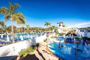 Ein Resort mit großzügigem Poolbereich, Palmen und einem weißen Gebäude mit rotem Dach.