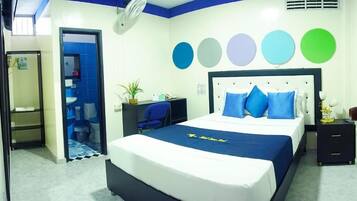 Habitación de hotel con una cama, un escritorio, una silla y una mesita. Se ve un baño por una puerta abierta.