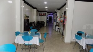 A dining area with blue chairs and tables, a sofa, and a kitchen in the background. - Hotel Luna Azul  (Florencia)