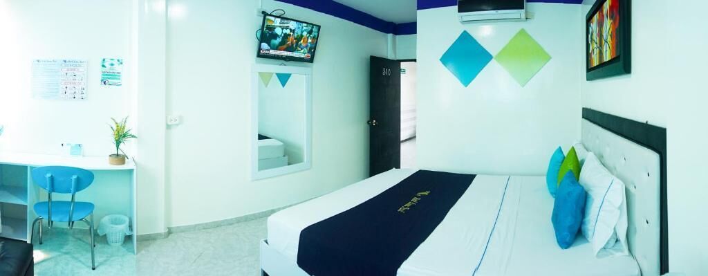 A hotel room with a bed, a desk, a chair, a TV, and a bathroom.