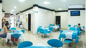 A hotel lobby with multiple tables and chairs, a reception desk, and a television screen on the wall. - Hotel Luna Azul  (Florencia)