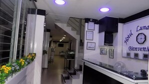 A hotel reception area with a staircase, a reception desk, and a wall with a clock and framed certificates. - Hotel Luna Azul  (Florencia)