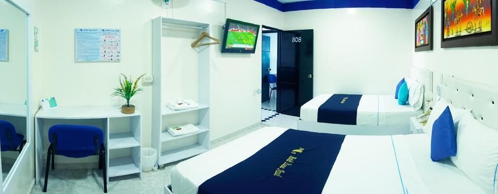 Habitación de hotel con cama, escritorio, silla, televisor y puerta.
