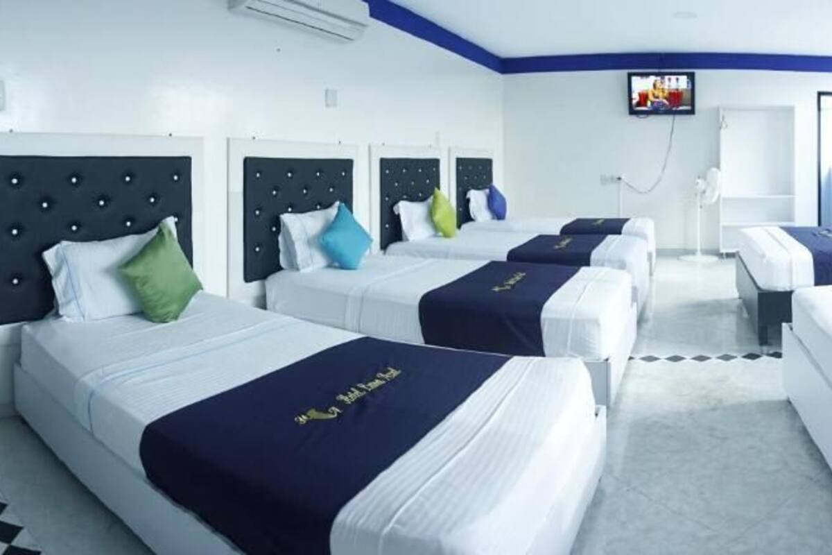 A hotel room with four beds, each with a headboard and pillows. There is a television mounted on the wall and a window providing natural light.