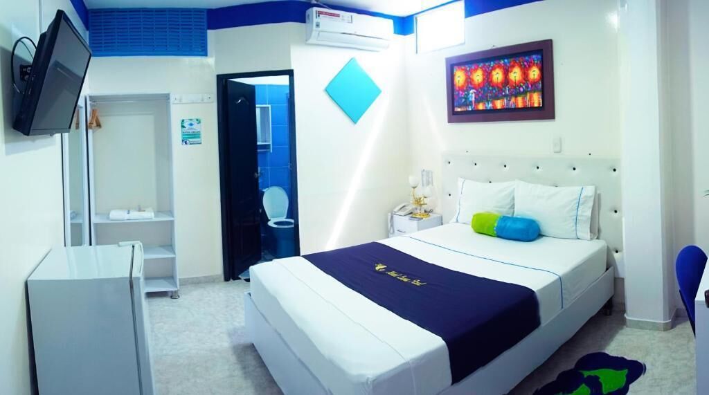 A hotel room with a bed, a desk, a chair, a TV, and an air conditioning unit.