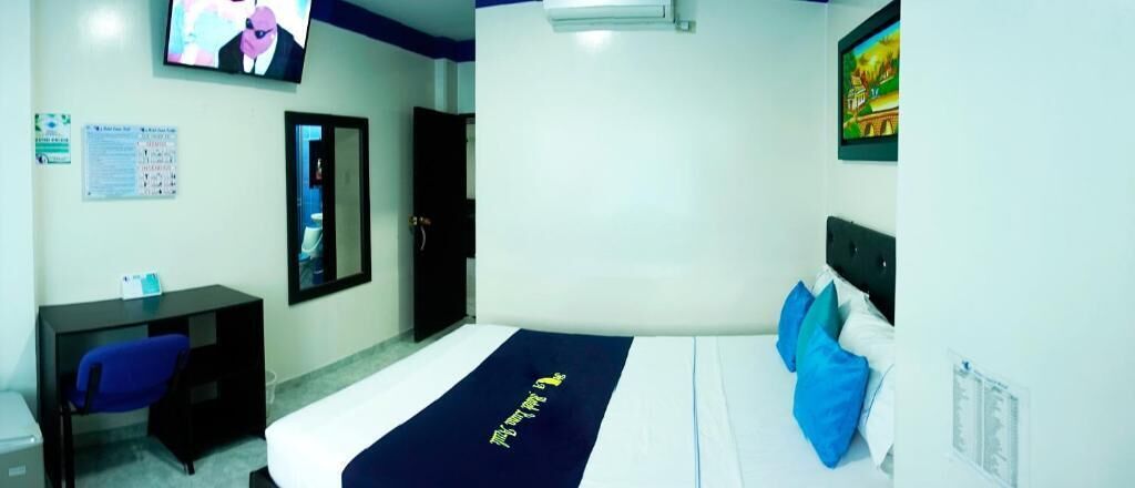 A hotel room with a bed, a desk, a chair, a TV, and a door.