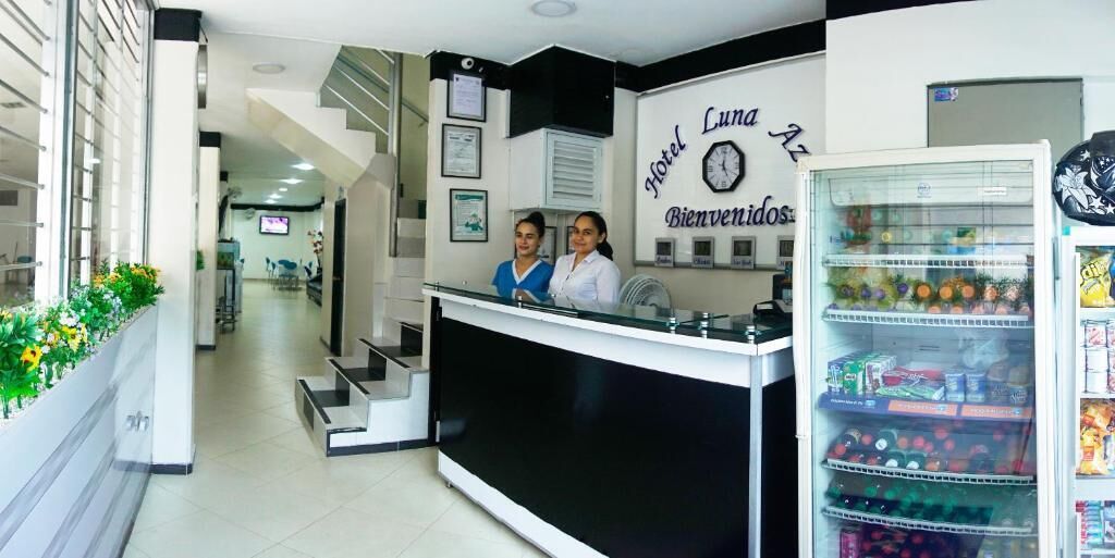 A hotel reception area with a reception desk, a clock, and a refrigerator stocked with beverages.
