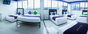 A hotel room with four beds arranged in a circular layout, large windows, and a tiled floor. - Hotel Luna Azul  (Florencia)