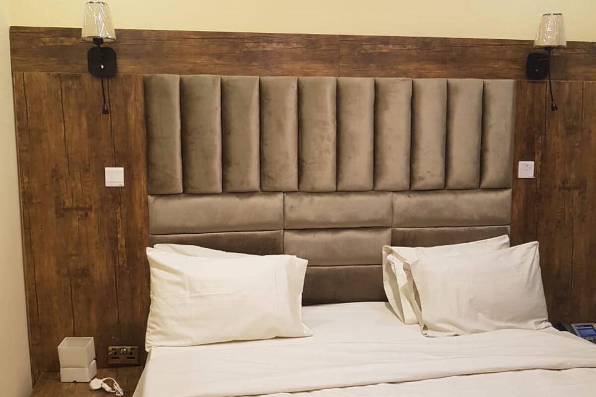 A bed with a wooden headboard, two pillows, a bedside table with a lamp, and a power outlet.