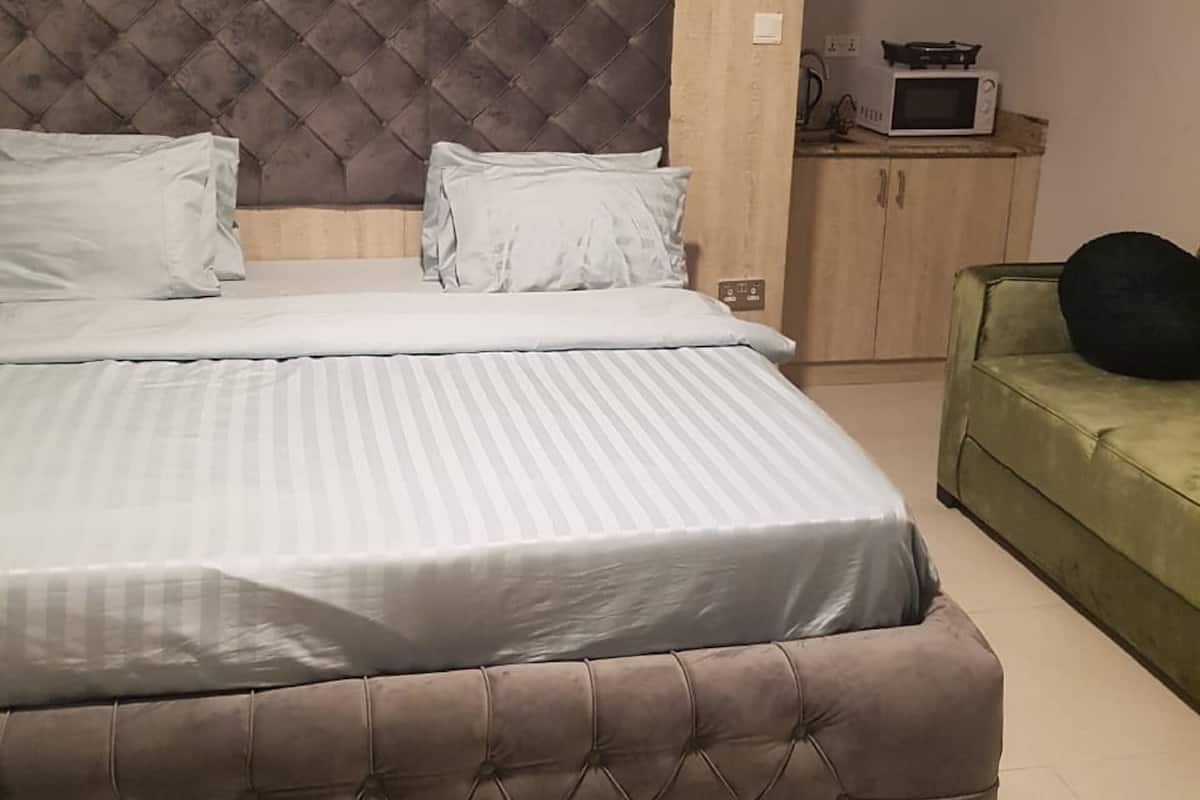 A bedroom with a large bed, a green sofa, a wooden headboard, a microwave, and a cabinet.