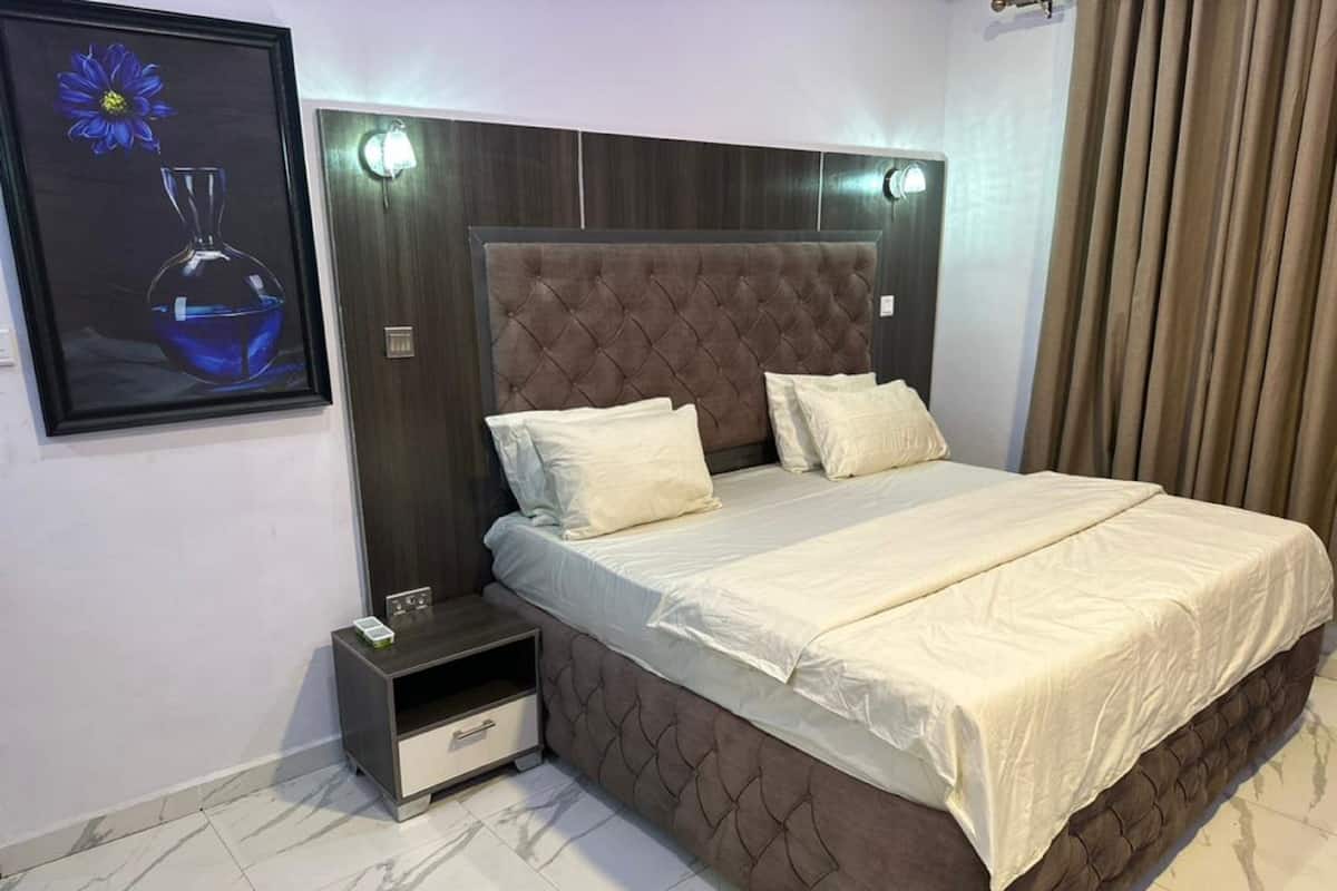A bedroom with a tufted headboard, a bed with white linens, a nightstand with a lamp, and a framed picture on the wall.