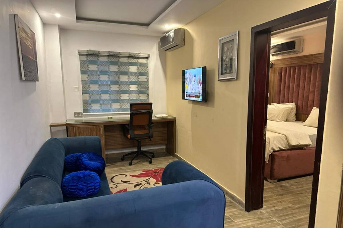 A hotel room with a blue sofa, a desk with a computer, a television, and a bed with a headboard.
