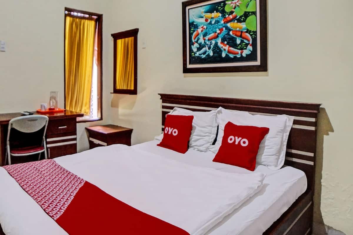 A hotel room with a bed, a desk, a chair, and a painting on the wall.