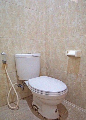 A toilet with a bidet attachment, a toilet paper holder, and a visible pipe on the floor. - OYO 92430 Anora Homestay (Medan)