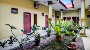 A courtyard with potted plants, a tiled floor, and a building with multiple doors and columns. - OYO 92430 Anora Homestay (Medan)