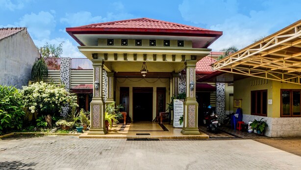 A building with a red-tiled roof, a covered entrance with columns, and a paved ground. - OYO 92430 Anora Homestay (Medan)
